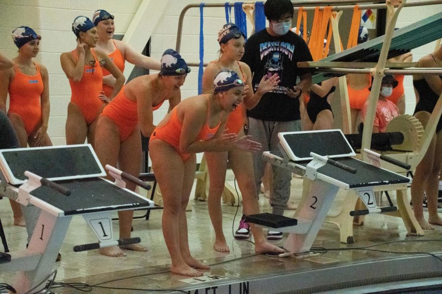 The varsity girls swim team cheers on their teammates from the pool deck.